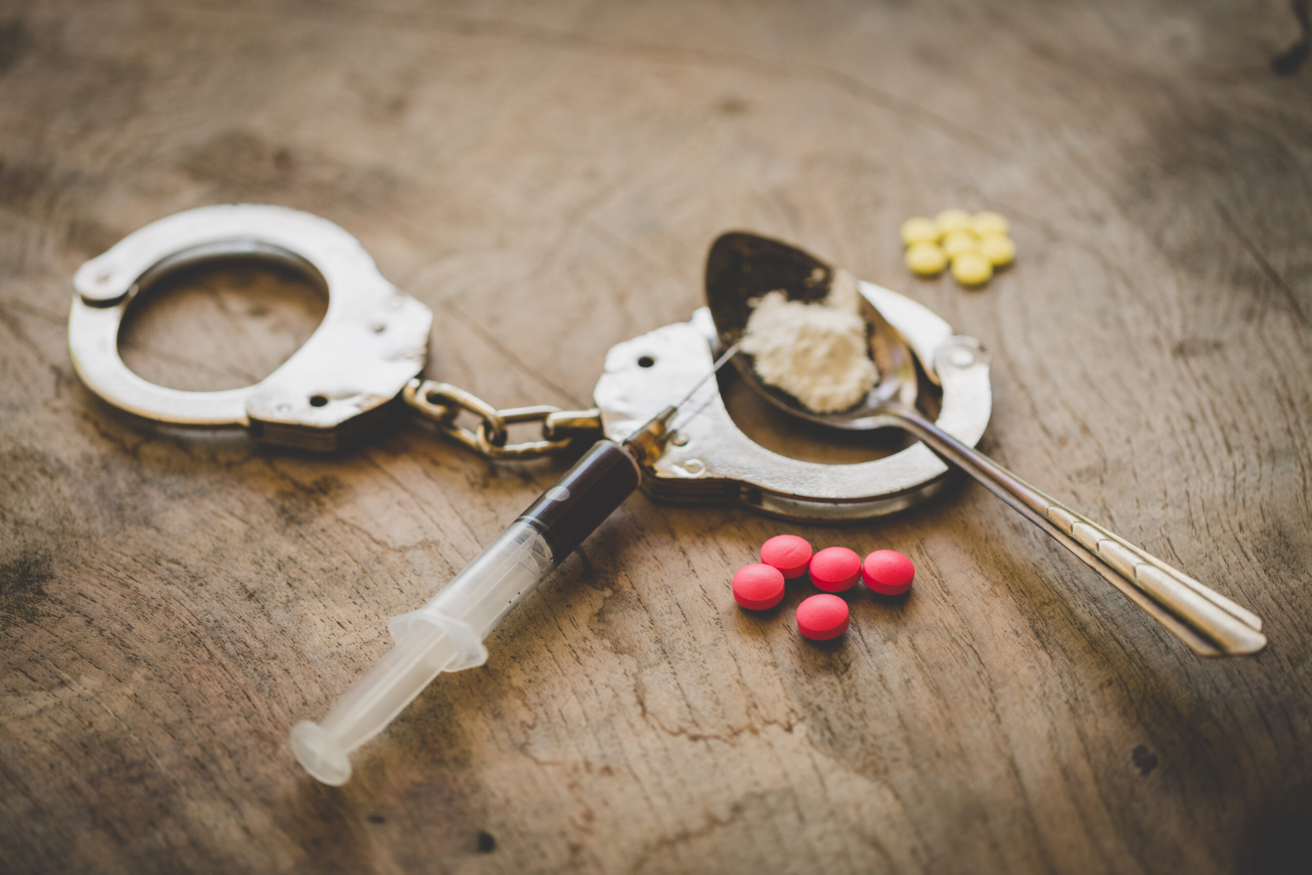 Handcuffs, drugs and syringes on wooden table