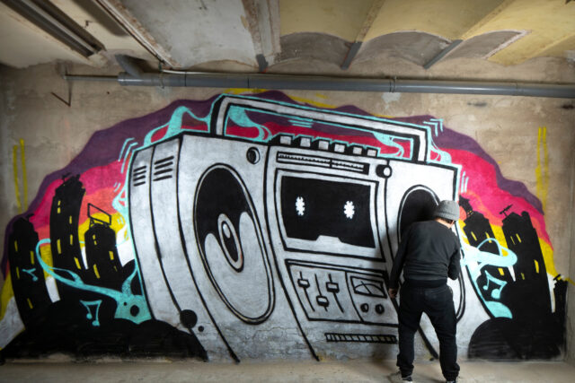 a graffii artist sprays art work of a boom box on a wall