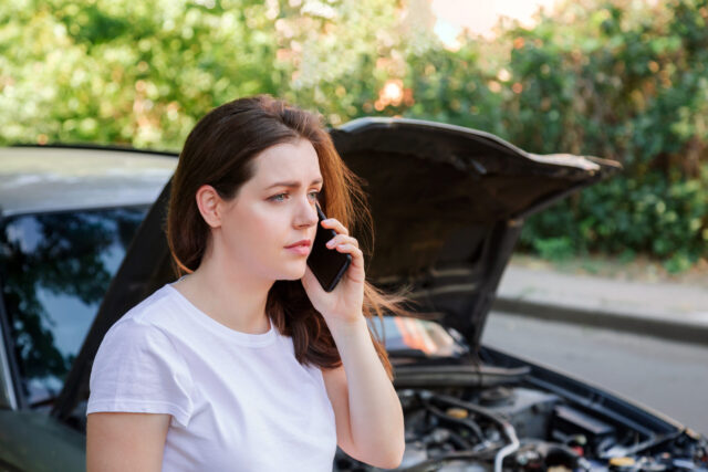 Portrait of frustrated young woman calling mobile phone for help Insurance service or ambulance after car accident. Woman in front of broken car with a mobile phone in hand
