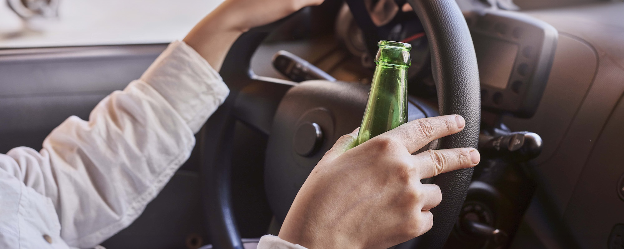 An unrecognizable female drinking beer while driving car