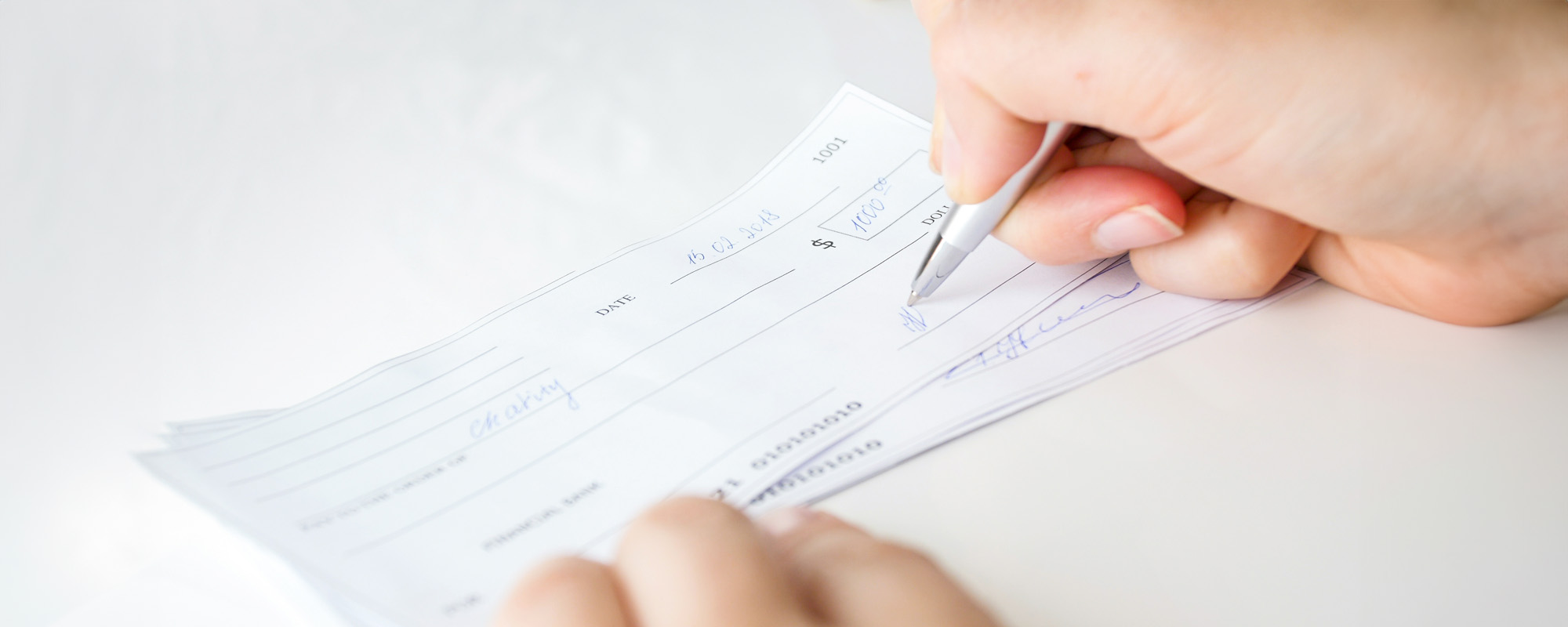 Closeup image of businesswoman putting her signature on personal bank cheque with pen