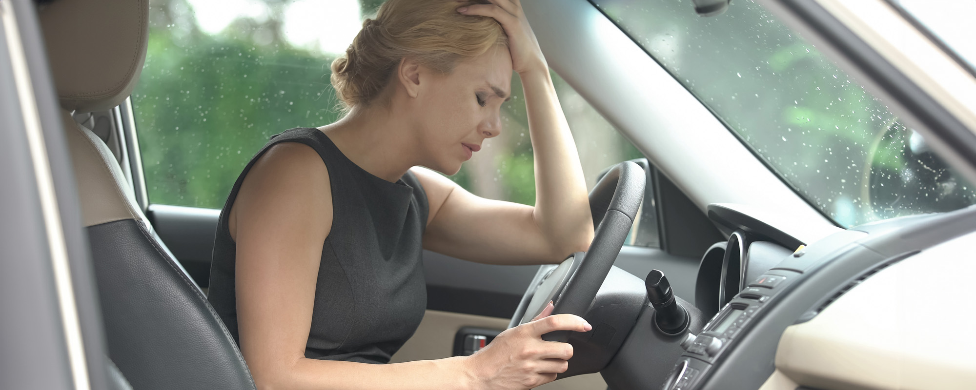 A woman in nice dress stressed with her head in her hand sitting in driver seat of vehicle after being pulled over without a drivers license; Rockland County Driving without a license attorney concept image