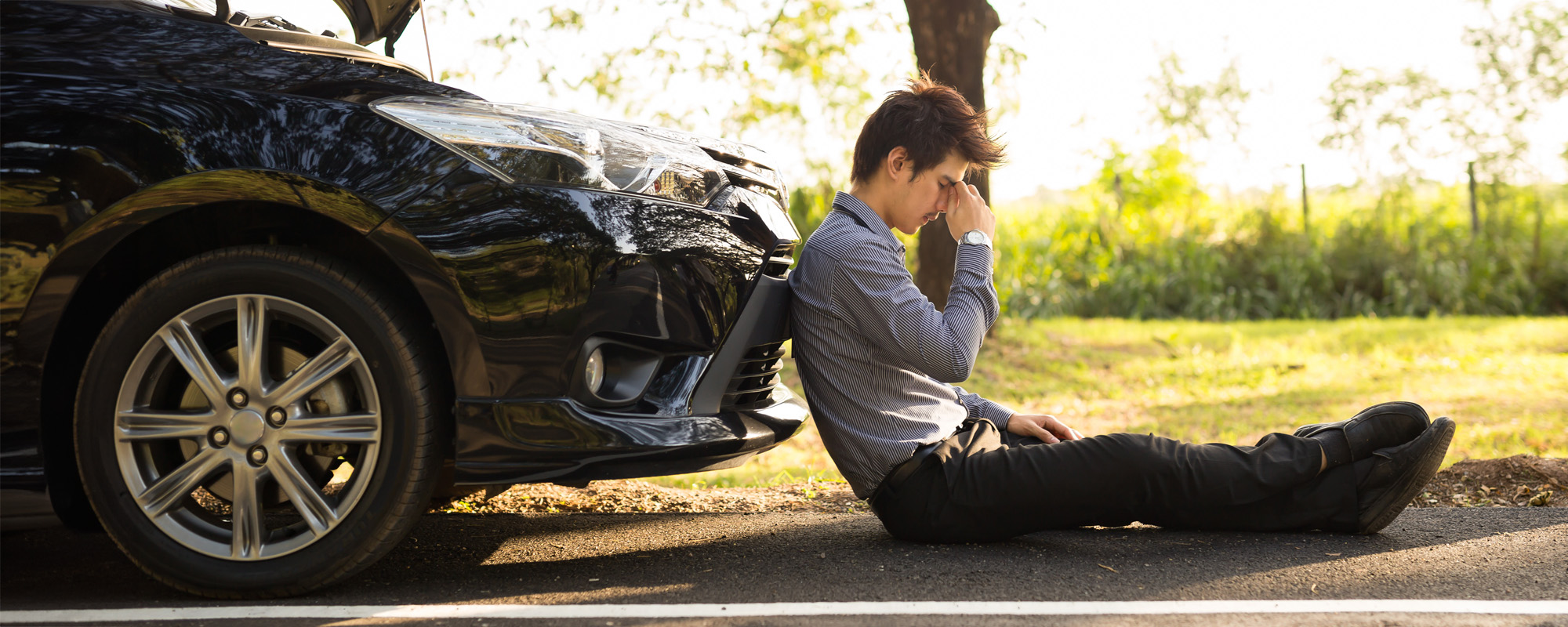 Full length of businessman with hands on head sitting by broken down car at countryside