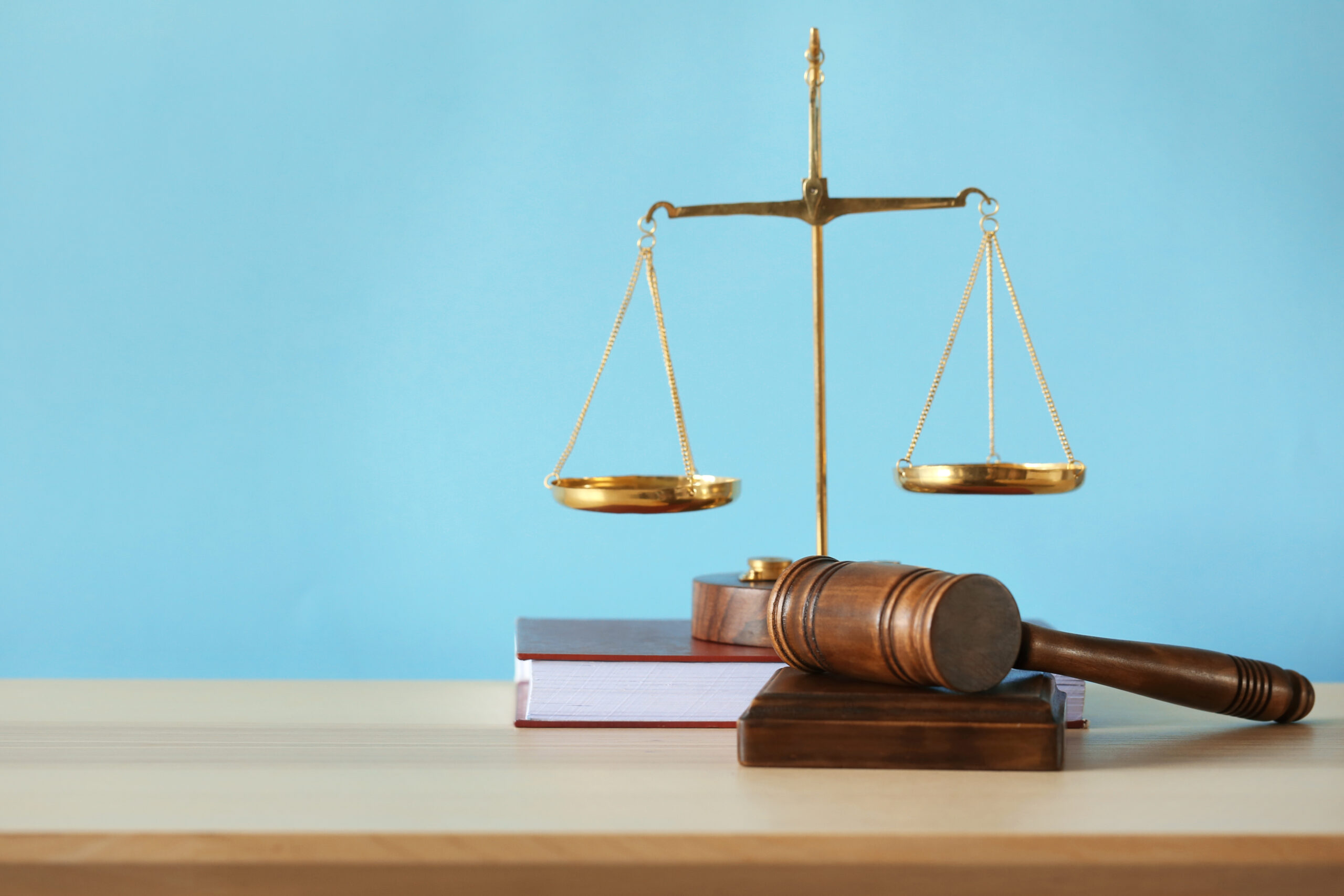 Justice scales, judge's gavel and book on wooden table and blue background